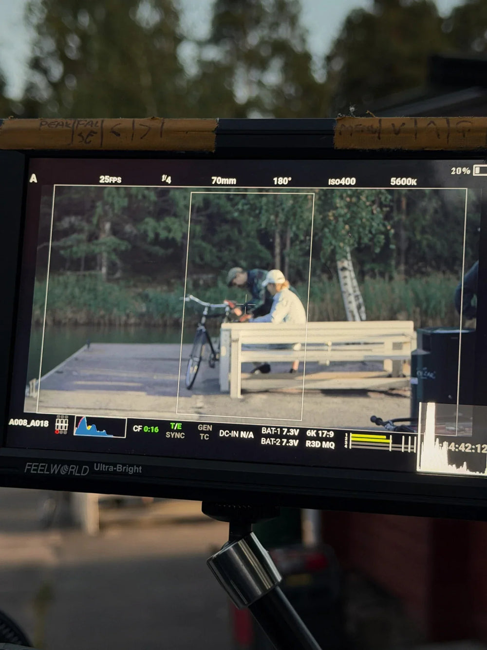 An image of a video screen showing a film director and a man sitting on a white bench by a pier
