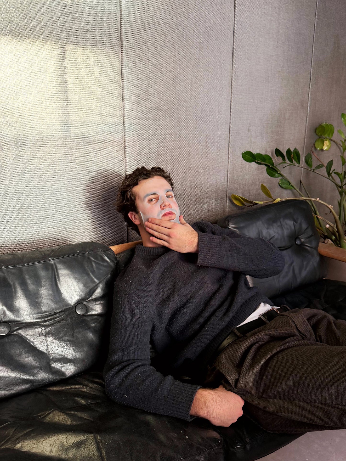 Man lying on a couch with a sheet mask, looking thoughtful.
