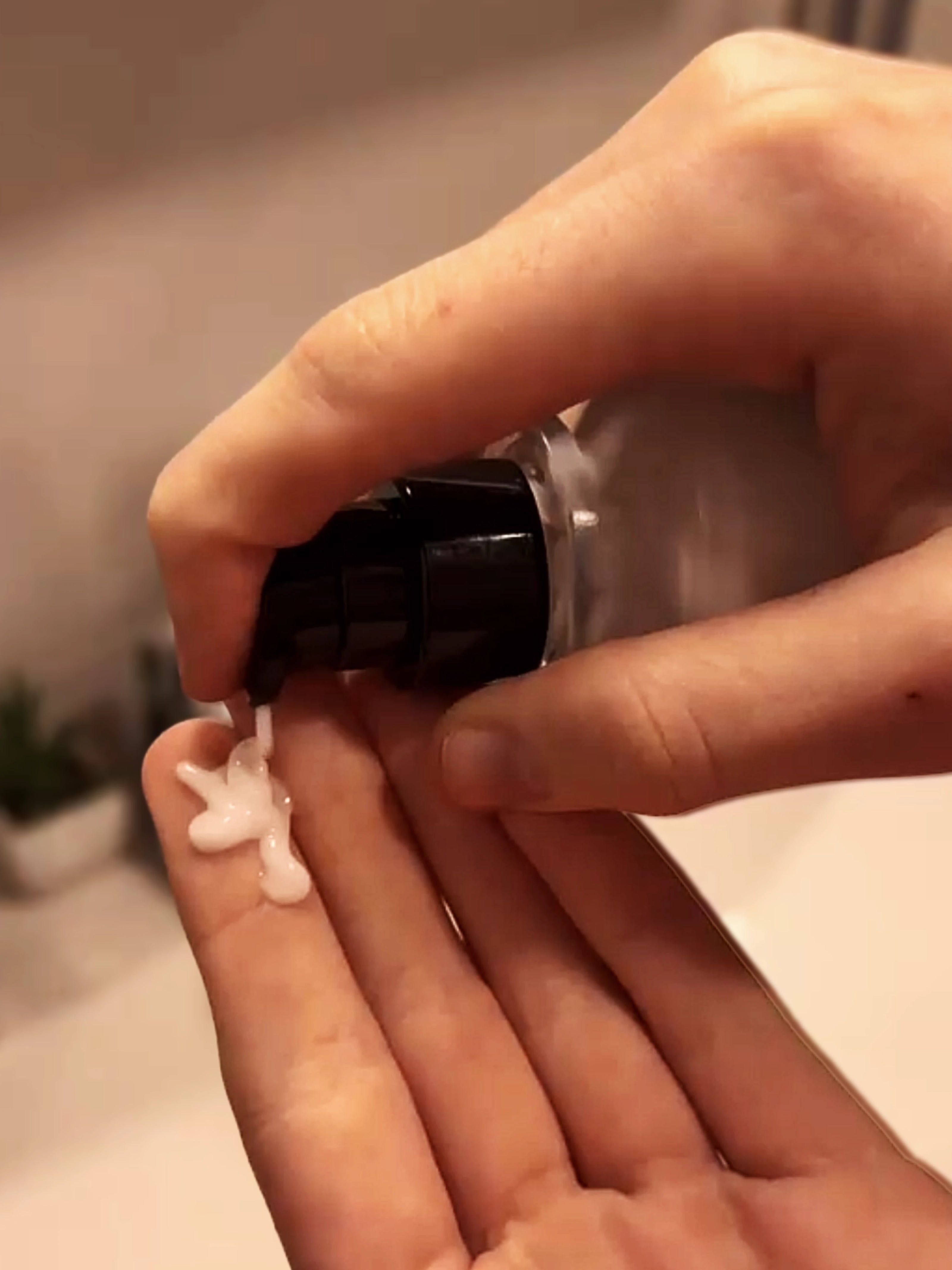 Hand applying a small amount of cream to another hand with a blurred background