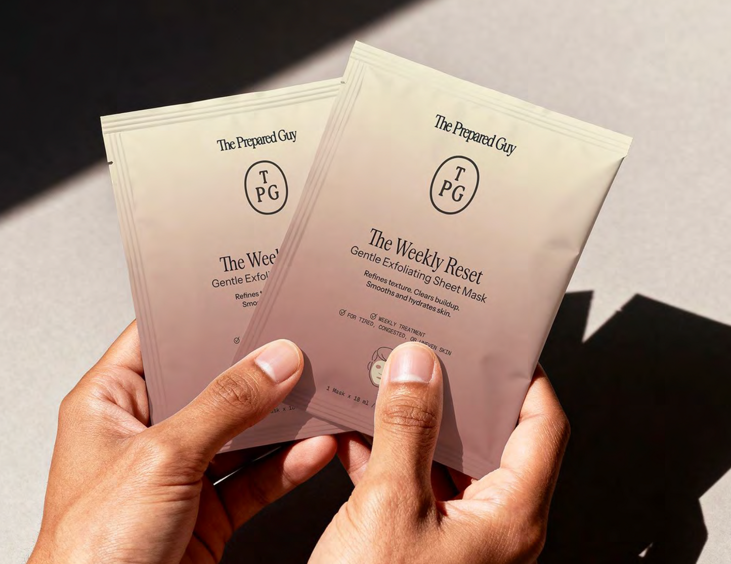 Two 'The Weekly Reset' The Prepared Guy sheet masks held by a hand with a neutral background