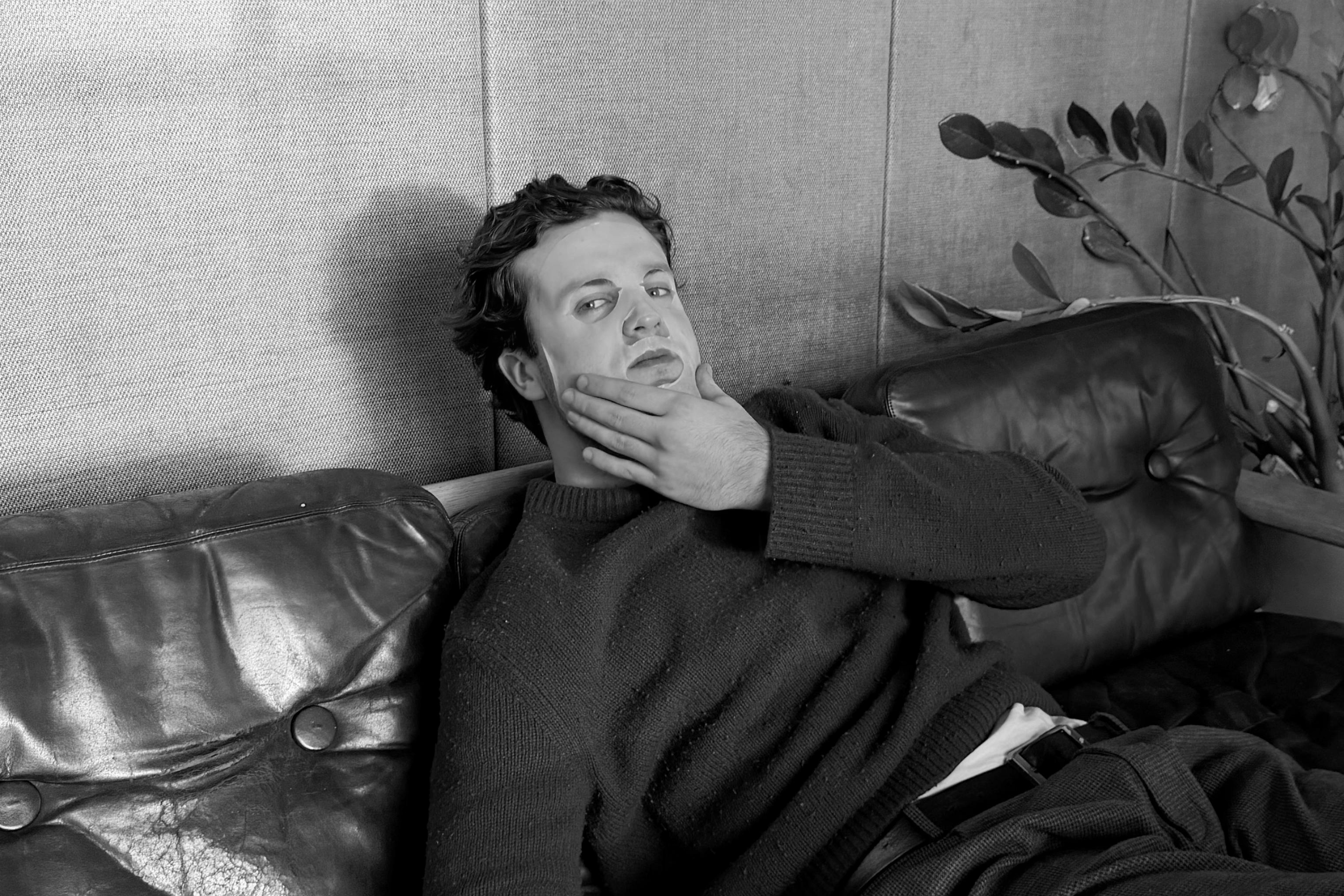 Man sitting on a leather couch with a pensive expression, black and white photo.