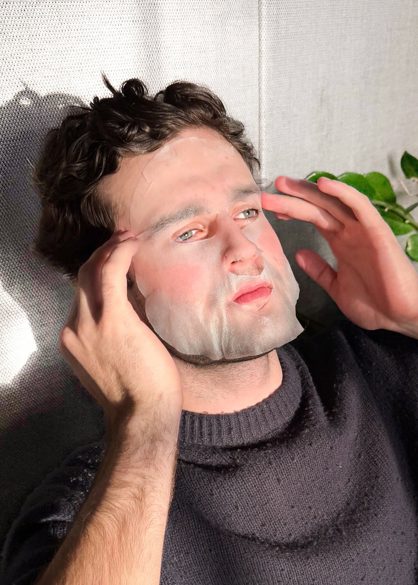 Person applying a face mask indoors with plants in the background