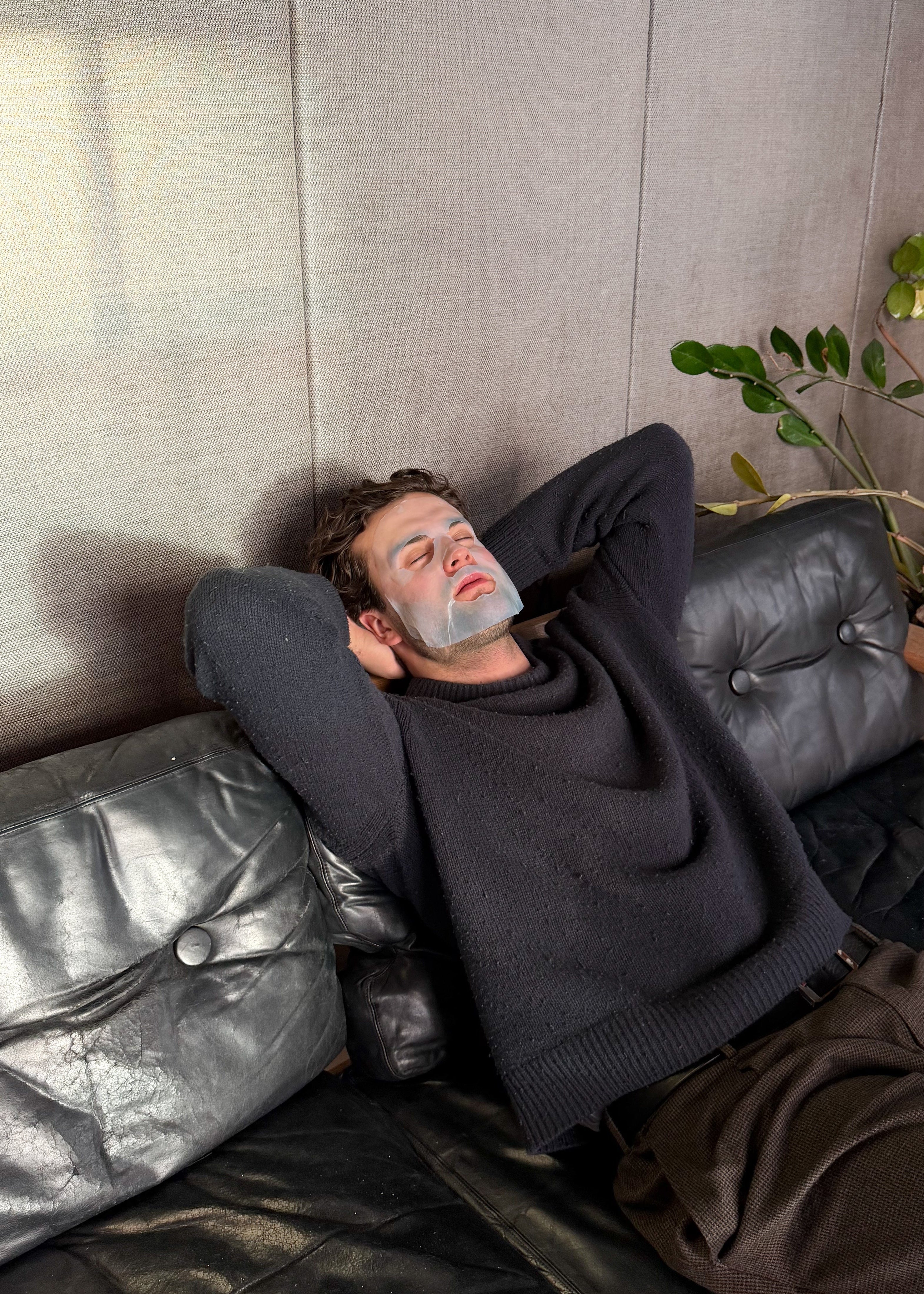 Man lying on a couch with a face mask, surrounded by a neutral-toned room.